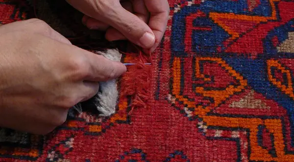 Mani che riparano un tappeto scolorito con ago e filo, un rimedio per ridare vita ai colori sbiaditi.