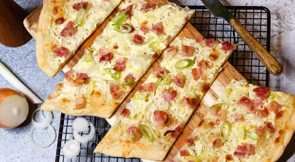 Flammkuchen-Rezept: knuspriger Teig mit Speck, Zwiebeln und Frühlingszwiebeln, bereit zum Genießen.