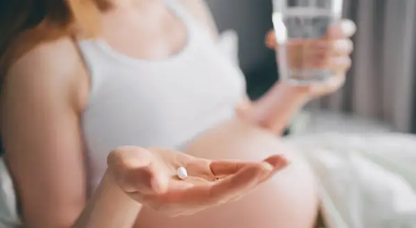 Ciężarna kobieta bierze tabletkę, by złagodzić objawy anginy. Dba o zdrowie swoje i dziecka.