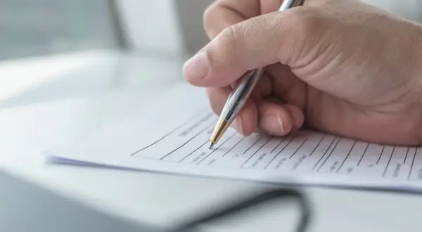 Dłoń pisze długopisem na kwestionariuszu osobowym dla pracownika.
