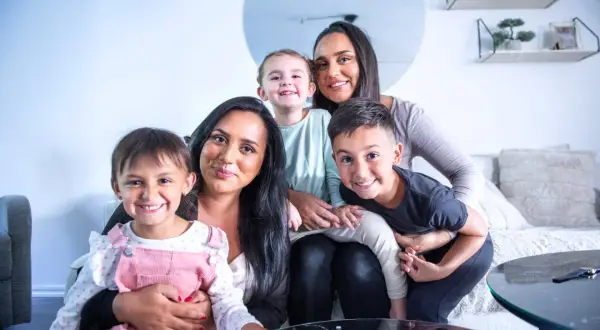 Familjen njuter av sitt hem efter en lyckad svensk villarenovering. Två mammor och tre barn ler glatt mot kameran.