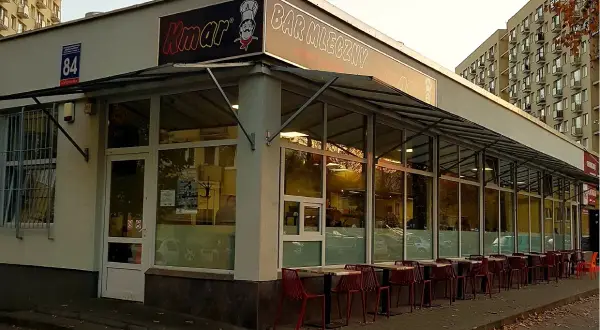 Bar mleczny Kmar z czerwonymi krzesłami przed wejściem.