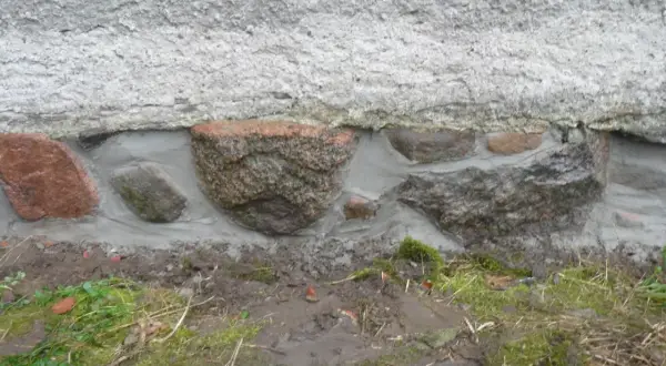 Das Feldsteinfundament wird mit Mörtel abgedichtet. Große Steine sind sichtbar, umgeben von frischem Mörtel, der die Lücken füllt.