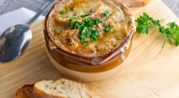 Un bol de soupe à l'oignon gratinée, avec du fromage fondu et des croûtons, garni de persil frais. Servi avec des tranches de pain grillé.