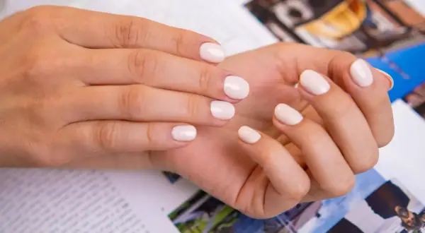 Delikatne, modne paznokcie french w odcieniu nude. Dłonie spoczywają na magazynie z kolorowymi zdjęciami.