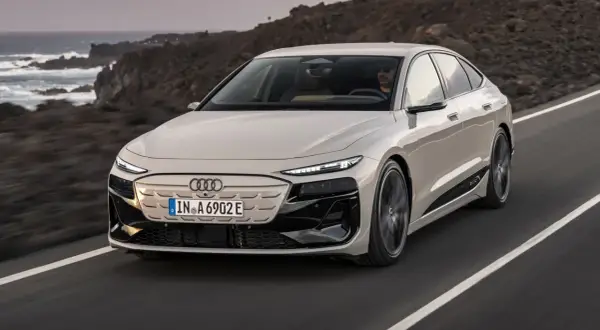 Elegancki Audi A6 e-tron w kolorze jasnego beżu przemierza malowniczą, skalistą trasę nad oceanem.