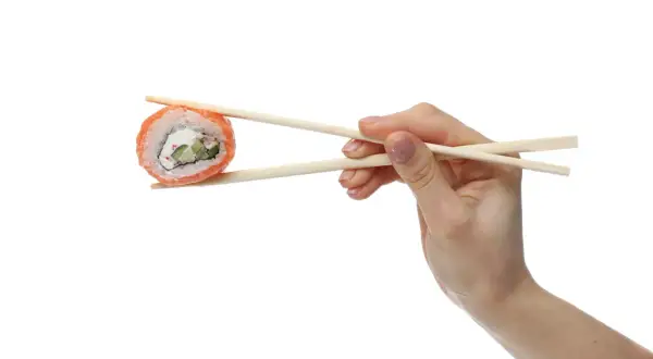 Dłoń trzymająca pałeczkami do sushi kawałek rolki sushi z łososiem i serkiem.