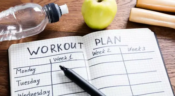 Plan na **full body workout** w zeszycie, obok jabłka, butelki wody i hantli.