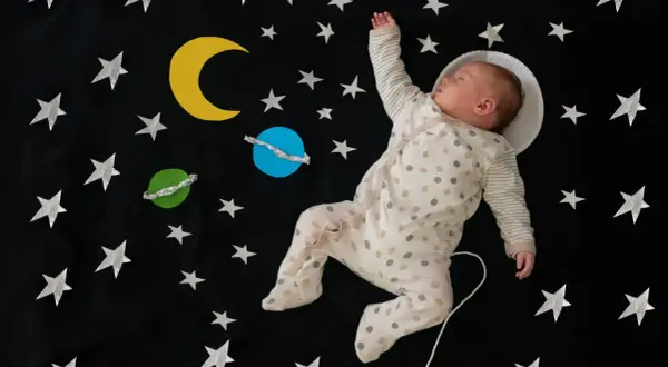 Śpiące dziecko w piżamce w kropki, otoczone gwiazdami i planetami, jakby leciało w kosmos. Ach śpij kochanie tekst pasuje do tej sceny.