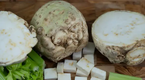 Knollensellerie-Rezepte für eine herzhafte Hauptspeise: Ein ganzer Knollensellerie, halbiert und gewürfelt, mit Staudensellerie auf Holzuntergrund.
