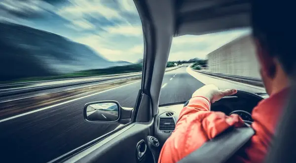 Kierowca w pomarańczowej kurtce jedzie autostradą. Widać rozmycie drogi i krajobrazu, co sugeruje dużą prędkość. Wymaga to ostrożności, a nawet szczególnej ostrożności.