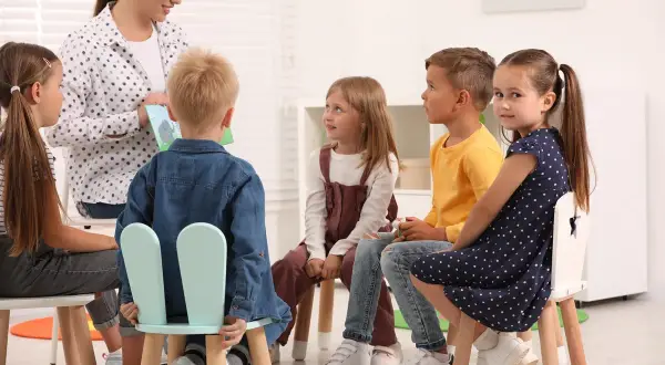 Nauczycielka czyta dzieciom książkę. Grupa przedszkolna liczy 6 dzieci.