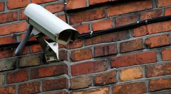 Caméra de surveillance blanche fixée sur un mur de briques. Comment reconnaître une caméra factice ? Cherchez l'absence de câbles ou de voyants lumineux.