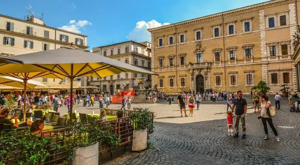 Piazza animata con persone che passeggiano e si godono un caffè all'aperto, un assaggio delle serate Erasmus a Roma.