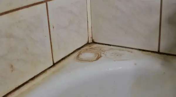 Coins de baignoire sales, avec des traces de javel sur le carrelage et des auréoles sur le blanc.