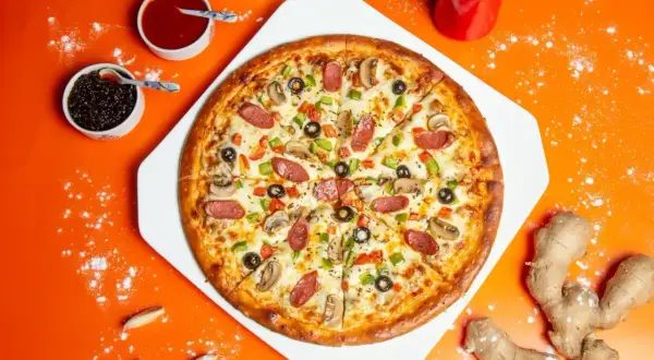Pyszna pizza z kiełbasą, pieczarkami i oliwkami. Obok sosy, czosnek i imbir – idealne składniki na pizzę.