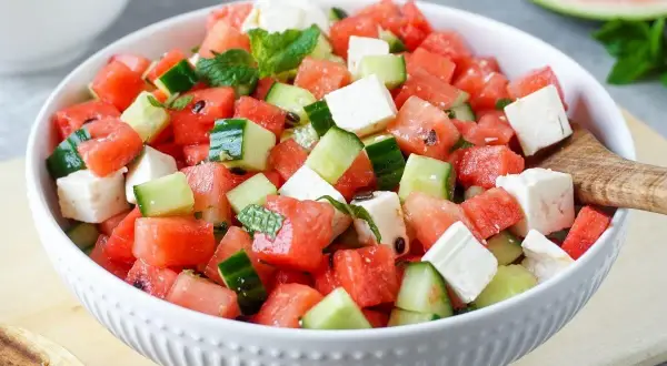 Erfrischender Melonensalat mit Mozzarella, Gurken und Minze in einer weißen Schüssel. Perfekt für heiße Tage!