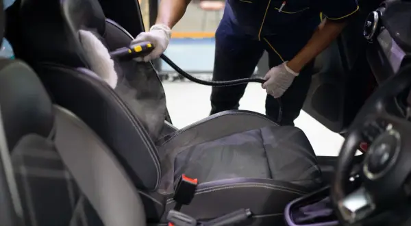 Profesional usando vapor para limpiar los asientos del coche. El vapor ayuda a eliminar manchas y desinfectar.