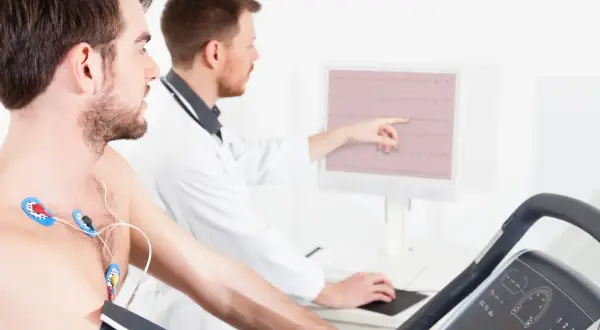 Un homme subit un test d'effort dangereux sur un tapis roulant, des électrodes sur la poitrine, tandis qu'un médecin surveille son rythme cardiaque sur un écran.