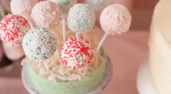 Bunte Kuchen am Stiel, verziert mit Perlen und Streuseln, auf einem grünen Podest arrangiert.