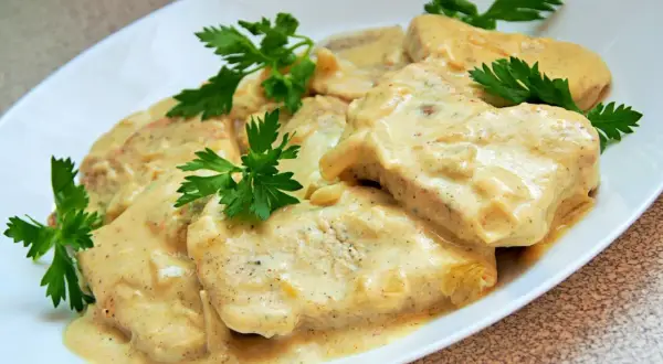 Pyszny filet z indyka w sosie śmietanowym, udekorowany natką pietruszki. Danie wygląda apetycznie i zachęca do spróbowania.