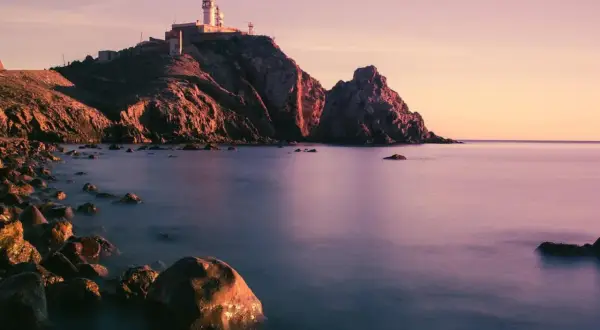 Faro en Cabo de Gata al atardecer, con rocas en primer plano y el mar en calma. Un lugar perfecto para disfrutar de la tranquilidad, como en el bar La Estrella.