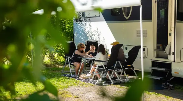 Family playing cards at a table outside a camper van on a sunny day.