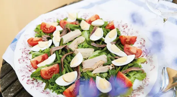 En härlig sallad nicoise med tonfisk, ägg, gröna bönor och tomater på en vacker tallrik.