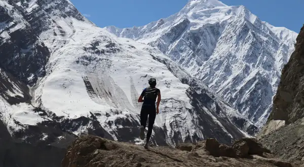 Perrine Fages court sur un sentier rocailleux face à des montagnes enneigées majestueuses sous un ciel bleu éclatant.