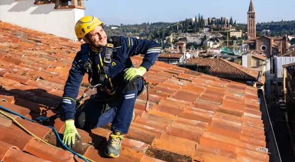 Operaio in corda per la riparazione tetto casa, con vista panoramica sulla città.