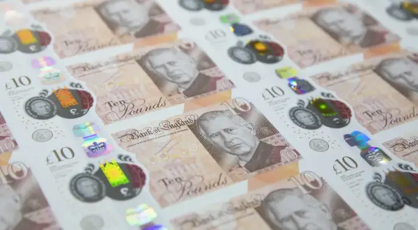 Nowe funty brytyjskie banknoty z wizerunkiem króla Karola III, w tle widać poprzednie banknoty z królową Elżbietą II.