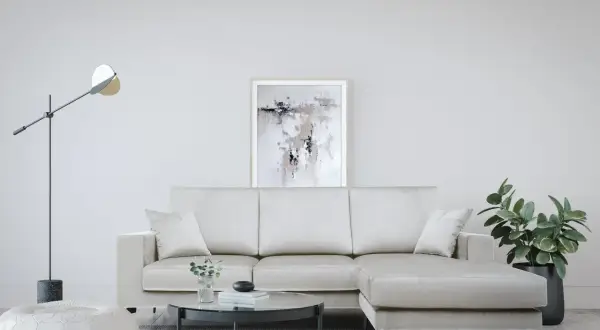 Divano angolare color crema, con tavolino rotondo in vetro, pouf bianco e quadro astratto. Le misure divano angolare sono perfette per questo spazio.