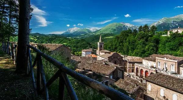 Borgo pittoresco nei Monti Sibillini, cosa vedere: tetti in cotto, campanile e montagne verdi.