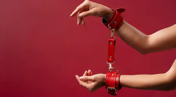 Czerwone kajdanki na nadgarstkach, idealne na początek przygody z bdsm. Delikatne ruchy dłoni sugerują eksplorację.