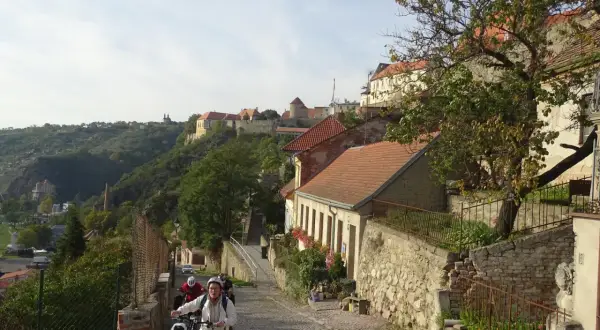 Radfahrer erkunden eine Kopfsteinpflasterstraße in Znaim, Tschechien, mit historischen Gebäuden und einer Burgruine im Hintergrund.
