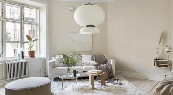 Ljust vardagsrum med en vit soffa, fluffig matta och en stor taklampa. Naturinredning med växter och trädetaljer skapar en lugn atmosfär.