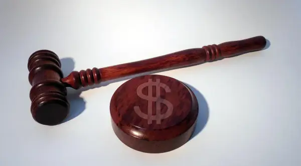 Młotek sędziowski z symbolem dolara na drewnianej podstawie. UFG kara za brak OC może być wysoka.