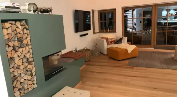 Gemütliches Wohnzimmer im modernen Landhausstil mit Kamin, Holzfußboden und großen Glasfronten.