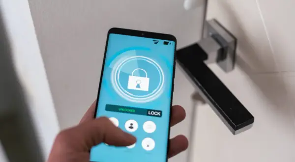 Dłoń trzyma smartfon z aplikacją do zdalnego sterowania zamkiem. Wygodny self check-in bez klucza.