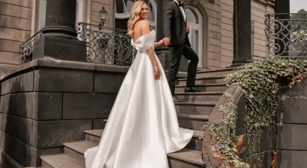 Brautpaar auf Treppe, sie trägt ein elegantes weißes schleppe brautkleid, er im schwarzen Anzug.
