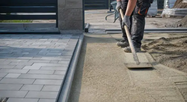 Pracownik równa podsypkę pod kostkę, przygotowując teren pod nową nawierzchnię.