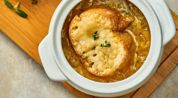 Soupe à l'oignon grand mère réconfortante, gratinée avec du pain et du fromage fondant, servie dans un bol blanc sur une planche en bois.