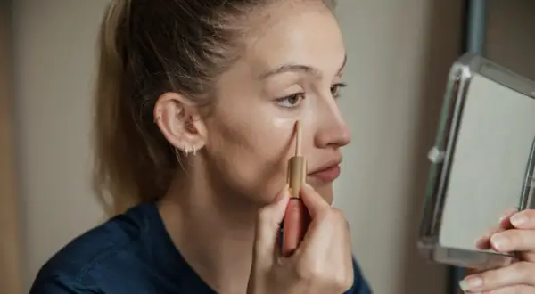 Ragazza applica correttore sotto l'occhio, un passo per capire il colore del correttore online.