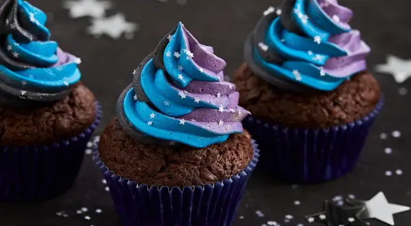 Drei Schoko-Cupcakes mit blau-lila Sternen-Frosting, inspiriert von einem Galaxie-Cupcake-Rezept.