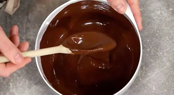 En sked rör i en skål med glansig choklad. Perfekt för ett enkelt ganache recept.