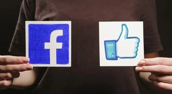Dwie ręce trzymają kartki z logo Facebooka i kciukiem w górę.