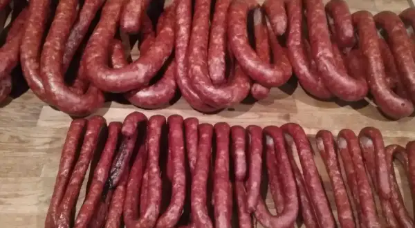 Dwie linie świeżych, czerwonych kiełbasek na drewnianym blacie. Zastanawiasz się, ile wołowiny do kiełbasy?