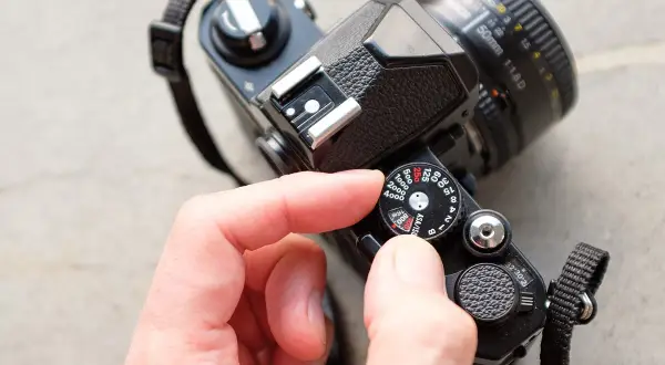 A hand adjusts the ISO dial on a vintage film camera, showing its mechanical controls.