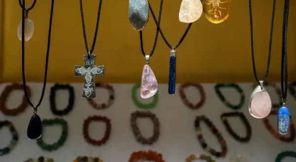 Wisiorki z kamieni, w tym krzyż z rybami, symbol siły kobiecej, i bursztyn ze skorpionem, wiszą na tle bransoletek.