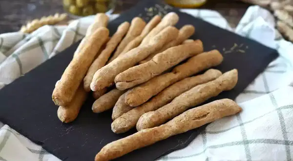 Une pile de gressins dorés, parfaits pour une recette gressin maison. Des olives et une boisson en arrière-plan.